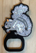 Magnetic metal bottle opener in the shape of a white squirrel holding a nut.