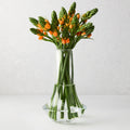 Clear, mouth-blown Marco Glass Vase with a modern shape, holding orange and green sculptural blooms.