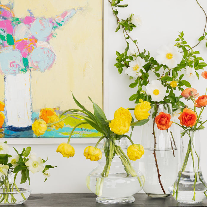 Clear mouth-blown glass Marco Vase with yellow tulips, alongside other vases with flowers.