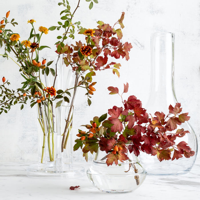 Clear mouth-blown glass Mario Vase, 7.1"H, with autumn branches and flowers, on a white surface.