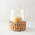 Medium glass hurricane with a woven natural hyacinth base and lit amber candle.