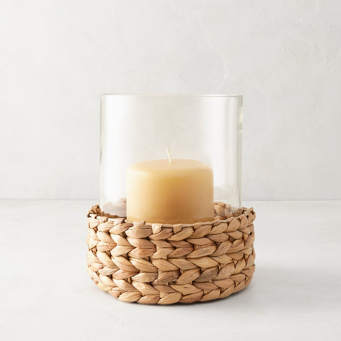 Medium glass hurricane with a woven natural hyacinth base and an amber candle.