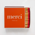Oversized orange "merci" boxed matches with white text and visible red-tipped matchsticks.