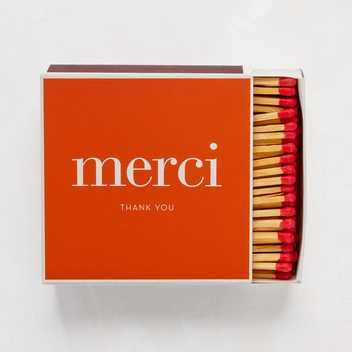 Oversized orange "merci" boxed matches with white text and visible red-tipped matchsticks.