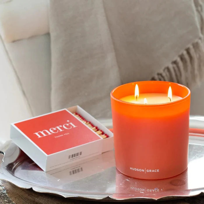 Hudson Grace "Merci" boxed matches and a lit orange candle on a silver tray.