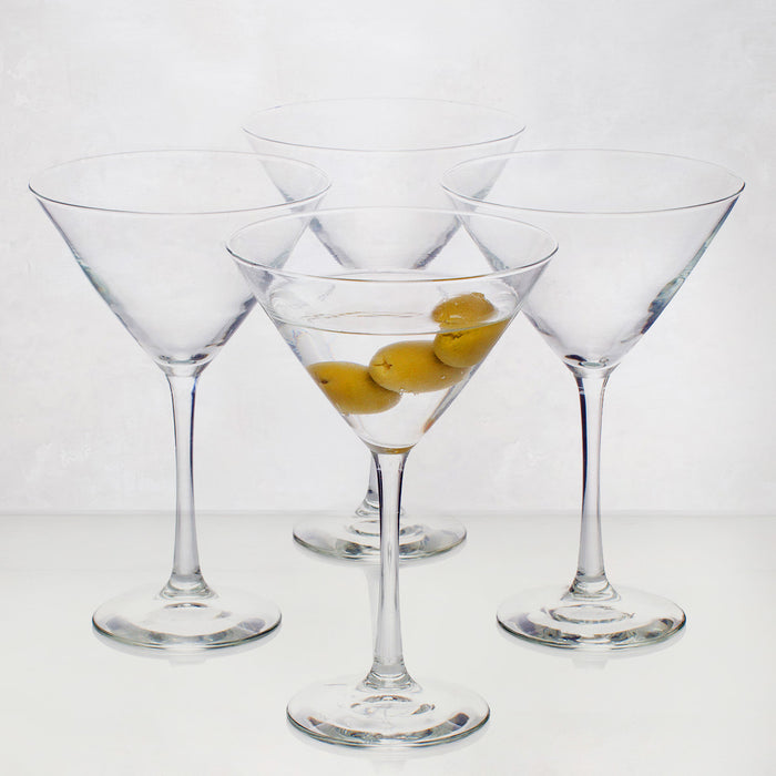 Four clear glass Midtown Martini glasses, one filled with a drink and three olives.