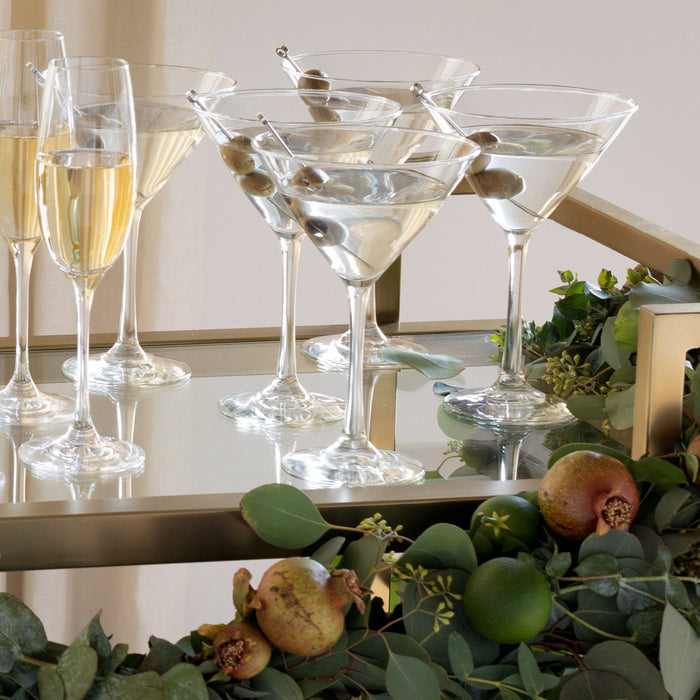 Clear glass Midtown Martini glasses with olives on a gold bar cart, alongside champagne flutes.