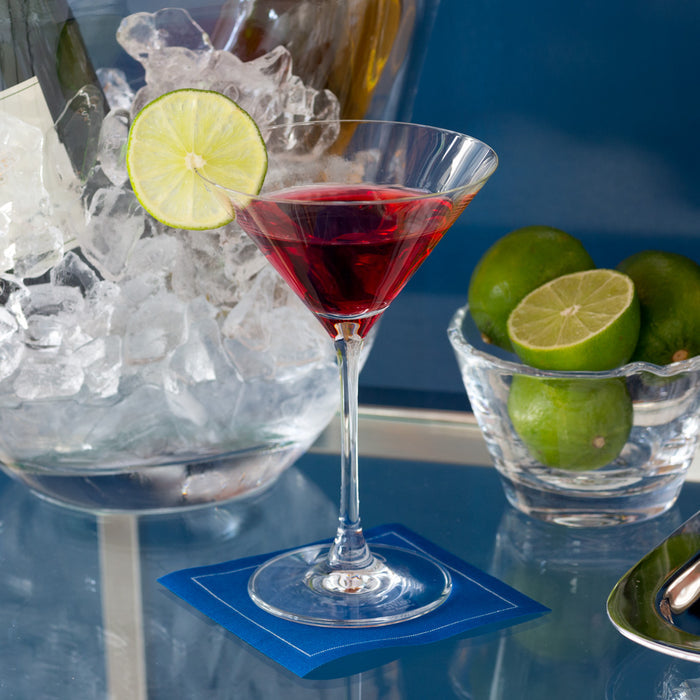 Clear glass Midtown Martini with red cocktail and lime slice on a blue coaster.