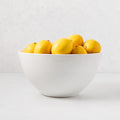 White ceramic serve bowl filled with bright yellow lemons.