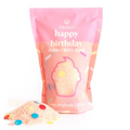 A pink stand-up pouch of musee 'happy birthday' Bubbly Bath Soak with a cupcake graphic and colorful confetti, shown on a white background with some bath soak spilled in front.