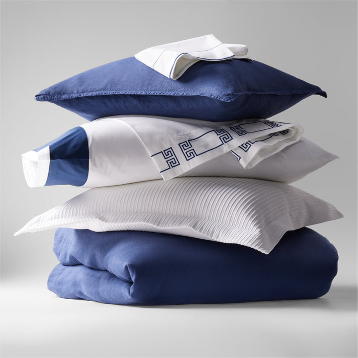 Stacked navy blue washed linen pillow shams, white pillows, and a folded navy linen duvet.