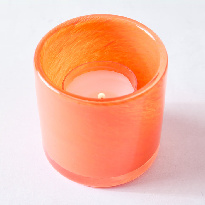 Orange votive glass candle holder with a lit white tea light candle inside.