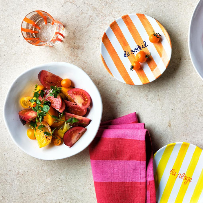 Organic ceramic low bowl in creamy white with heirloom tomato salad, next to striped plates and pink napkins.