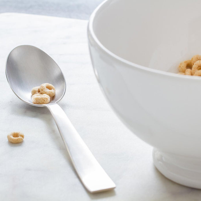HG Original creamy white ceramic footed bowl with a spoon holding cereal loops on a marble surface.