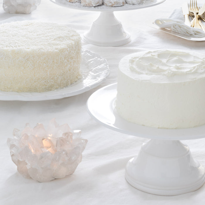 Small white ceramic pedestal cake stand with a frosted cake.