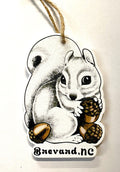 A laser cut wooden ornament in the shape of a cute white squirrel holding acorns, with the text 'Brevard, NC' on the bottom.
