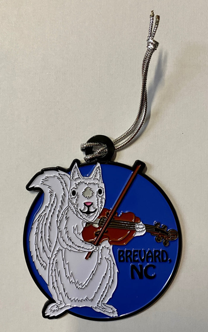 A metal ornament depicting a white squirrel playing a fiddle, with a blue background and the text 'BREVARD NC' on it.