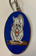 A metal ornament with a white squirrel with a Superman emblem on its chest. Blue background, with Brevard, NC on the log the squirrel is standing on.