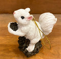 A white squirrel resin ornament perched on a pinecone with a gold-colored loop for hanging.