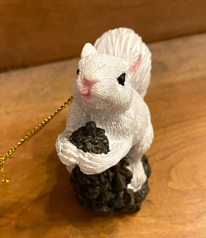White Squirrel sitting on a pine cone ornament with gold loop for hanging.