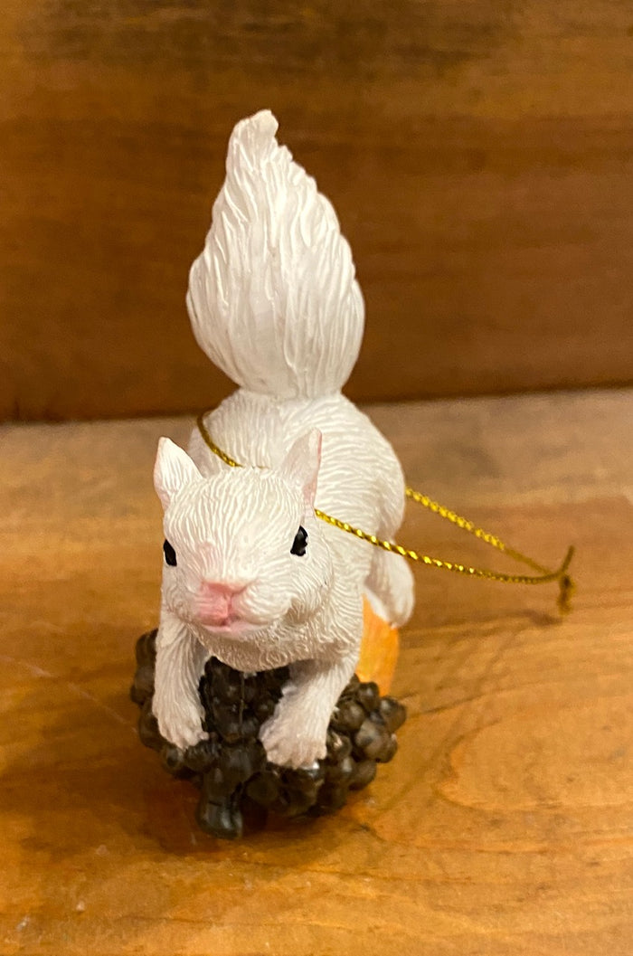 White squirrel sitting on top of an acorn ornament includes gold loop for hanging.