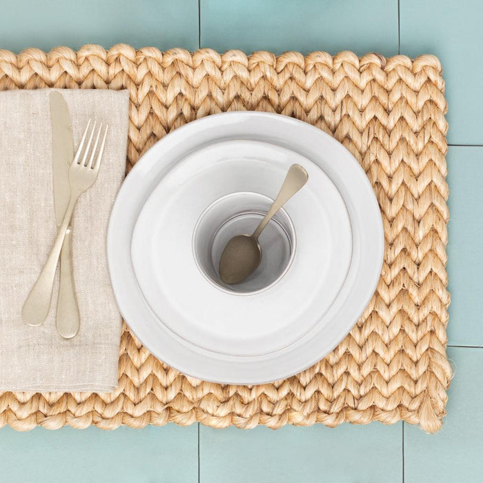 Oversized natural washed flax linen napkin, folded beside silverware and white plates on a woven placemat.