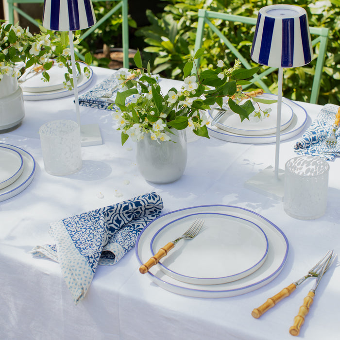 White stoneware salad plate with a hand-painted blue rim, set on a white tablecloth with blue patterned napkins.