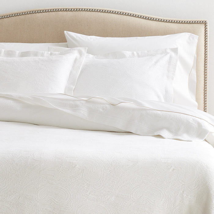 Paisley White Cotton Matelassé Shams, set of 2, on a bed with a beige headboard.