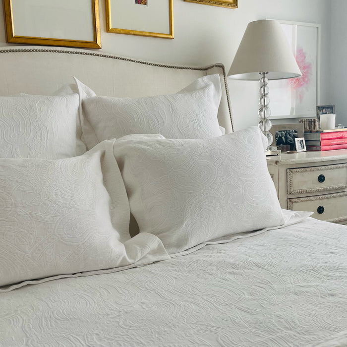 White cotton matelassé shams with subtle paisley pattern on a bed, with matching quilt.