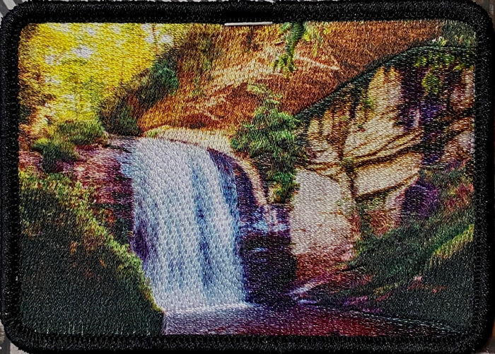 A patch featuring a colorful photograph of looking glass falls and surrounding foliage, stitched into a black fabric border.