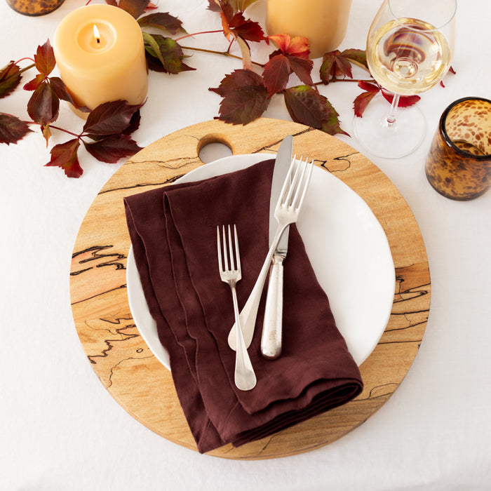 Pebble White ceramic salad plate on a round wooden charger with a brown napkin and silverware.