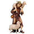 Hand-carved PEMA Kostner nativity shepherd wearing a brown coat and hat, carrying one sheep on his shoulders and standing beside another sheep, crafted in Val Gardena, Italy..