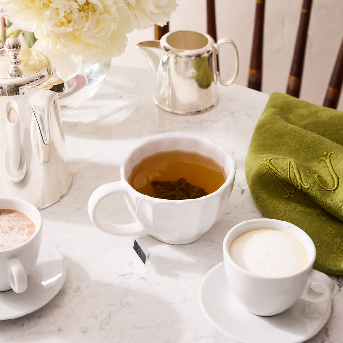 White Petal Stoneware Mug with tea, alongside other white mugs, silver creamer, and green napkin.