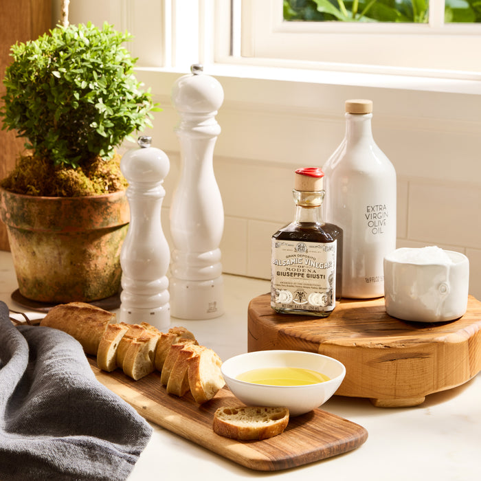 Two white lacquer Peugeot Paris pepper mills, 12" tall, on a kitchen counter with bread, olive oil, and vinegar.