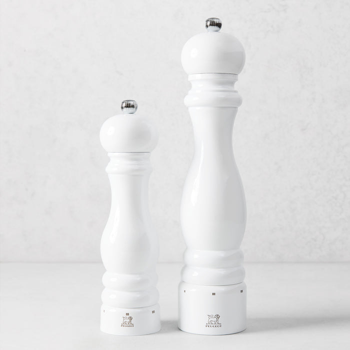 Two Peugeot Paris white lacquer beechwood pepper mills with chrome knobs on a light background.