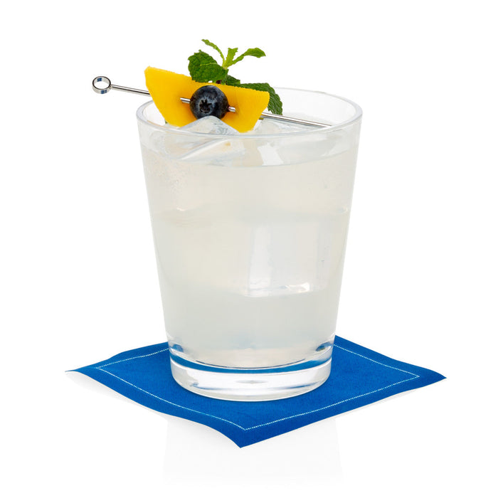 Clear acrylic double old-fashioned glass with a drink, garnished with mango, blueberry, and mint, on a blue napkin.