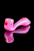 Pink glass pipe with a maple leaf design, reflected on a black surface.