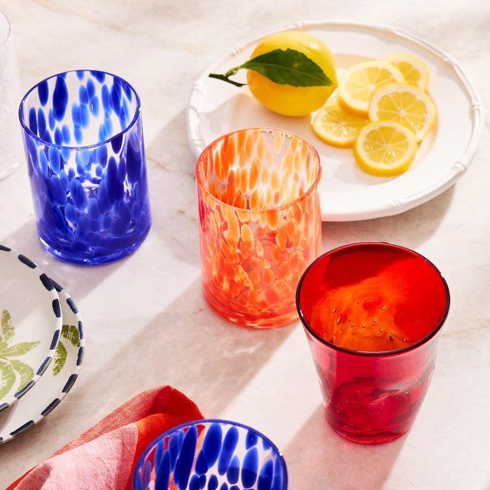 Red Henri Glass, 8 oz., with blue and orange speckled glasses, and lemons on a white plate.