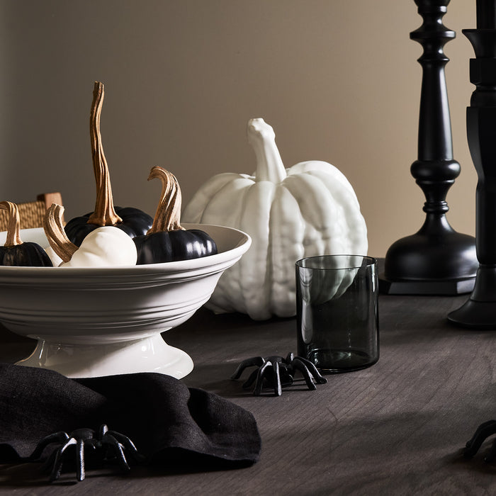 White ceramic footed bowl filled with black and white decorative pumpkins.