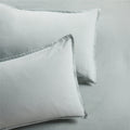 Two sage green washed linen pillow shams with a 2" flange and double-needle stitching.