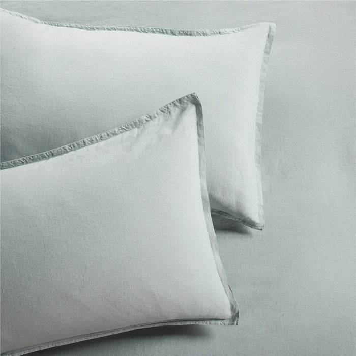 Two sage green washed linen pillow shams with a 2" flange and double-needle stitching.