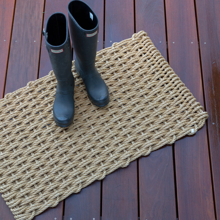 Sand braided rope doormat on a wooden deck with black rain boots.
