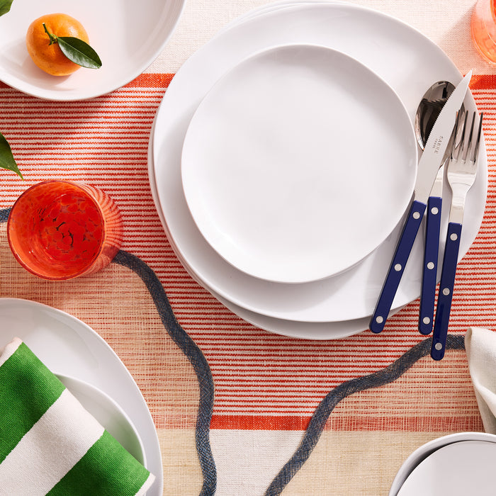 Sandia White 11" melamine dinner plate with a matte exterior and glossy interior, set on a striped tablecloth.