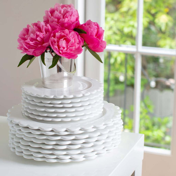 Stack of white ceramic scalloped salad plates with a small bucket of pink peonies on top.