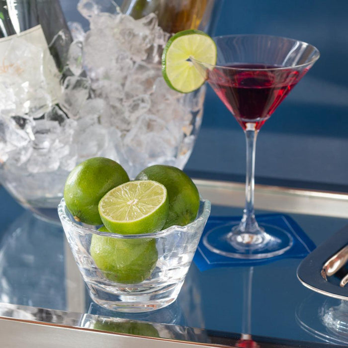 Clear, mouthblown glass breakfast bowl with scissor-cut top, holding whole and halved limes.