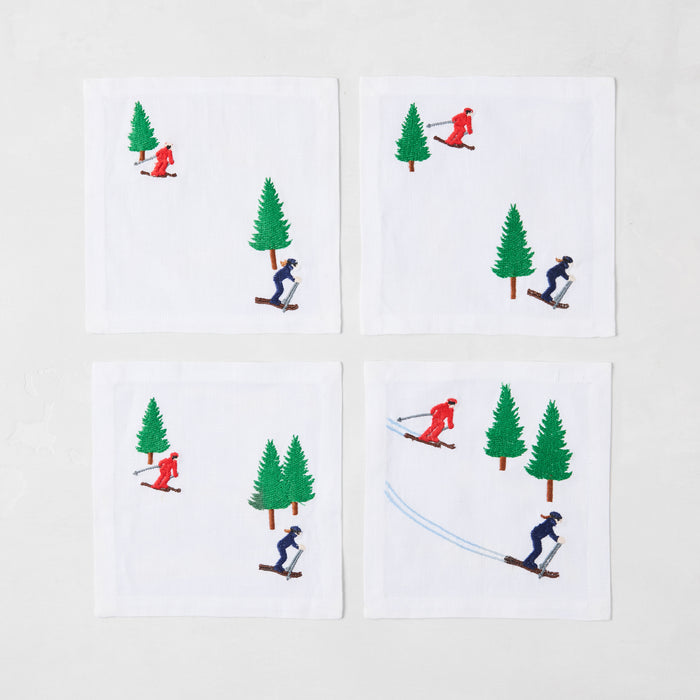 Set of 4 white linen coasters with embroidered skiers in red and blue, and green trees.