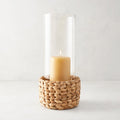 Small glass hurricane with a woven water hyacinth base and a lit amber candle.
