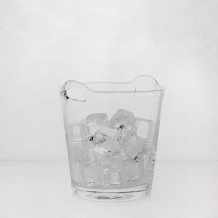 Small clear handblown glass ice bucket with integrated handles, filled with ice cubes.