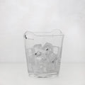 Small clear handblown glass ice bucket with integrated handles, filled with ice cubes.