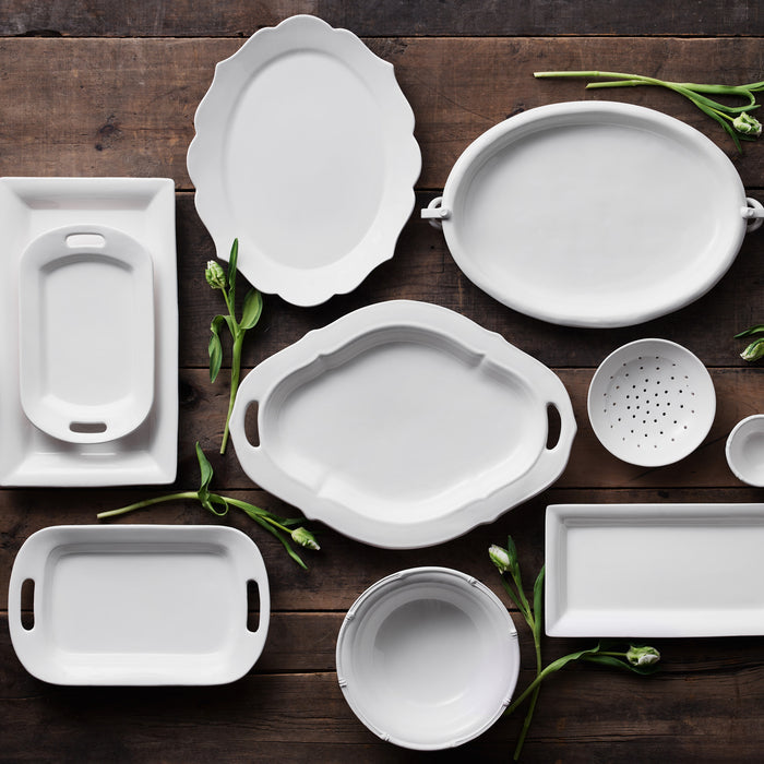 White ceramic Lucca rectangular serving platter, 17"L x 9"W, with other white platters on wood.
